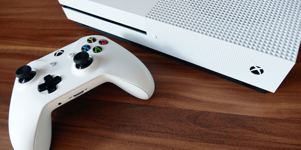 Biały kontroler Xbox z kolorowymi przyciskami obok białej konsoli Xbox na drewnianym blacie.