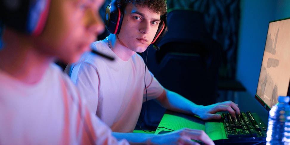 mężczyzna skupiony na grze komputerowej z słuchawkami, otoczony przez współgraczy w oświetlonym pomieszczeniu