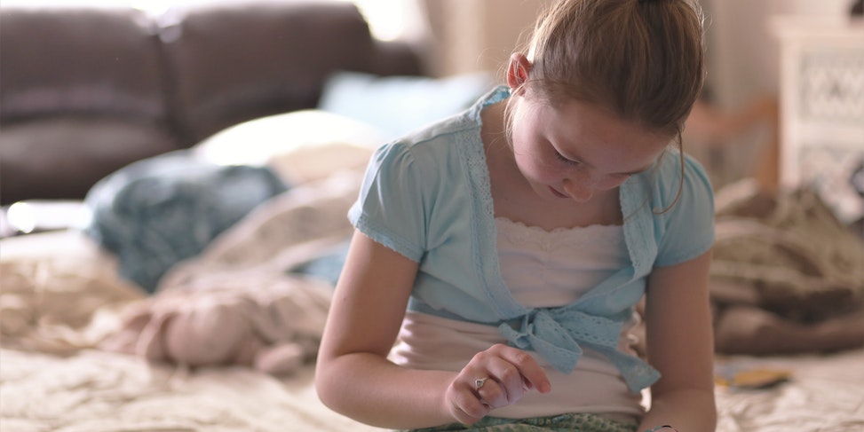 Dziewczynka siedzi na łóżku trzymając tablet w ręce